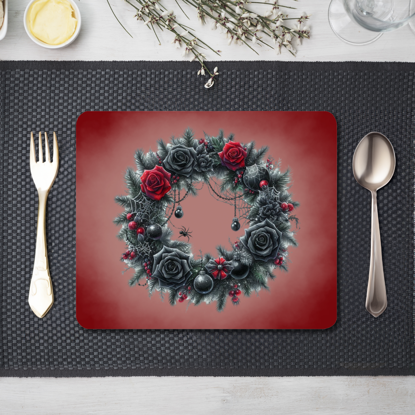 A table setting with cutlery and a red placemat with a smoky effect . A wreath with red and black roses, cobwebs and spiders is printed on the placemat 
